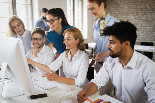 Productive, happy employees gather around a computer desk. Find out ways to increase employee productivity.