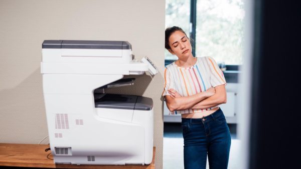 Women with her eyes closed leaning against wall with printer while dealing with printing issues